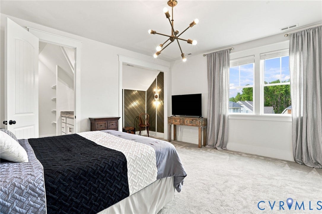 Spacious room featuring light-colored carpeting, white walls, and a modern brass chandelier