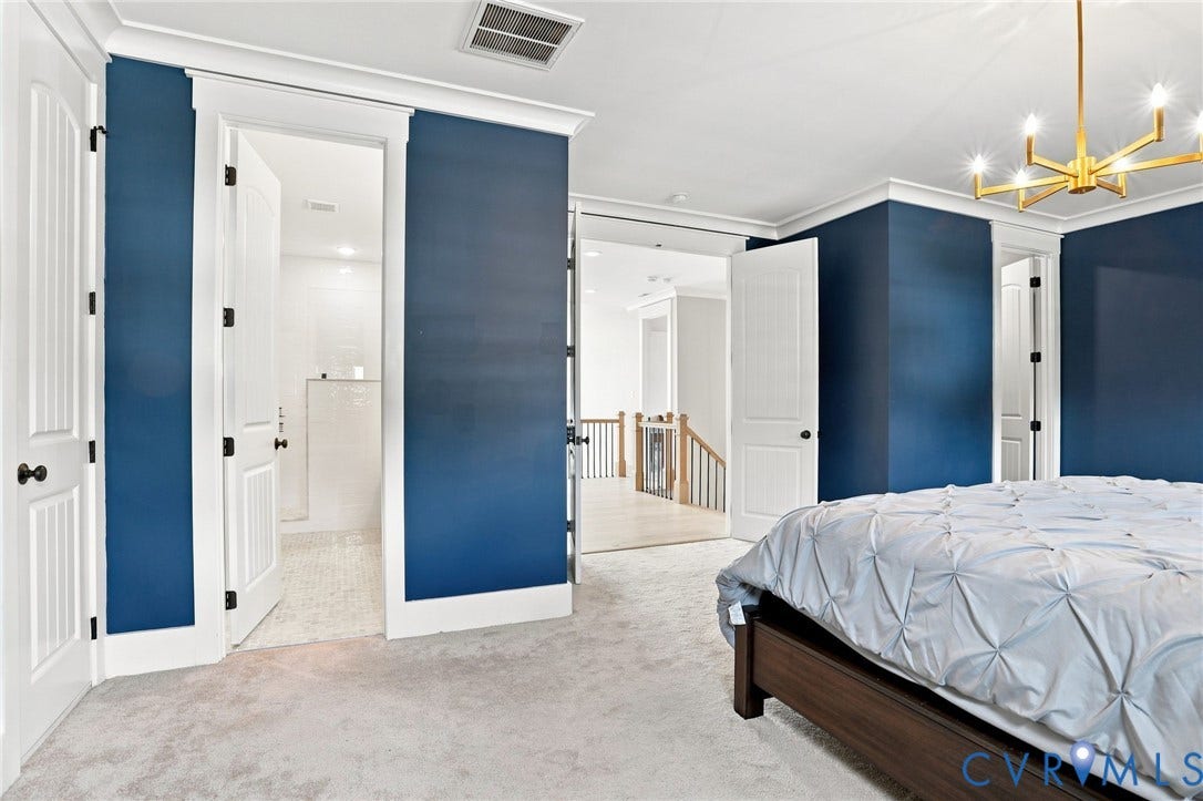 Carpeted room featuring a modern gold-finish chandelier, crown molding, and two panel doors with dark hardware