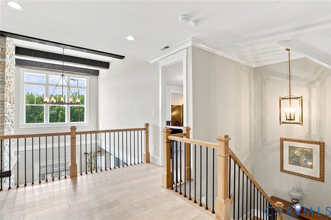 Upper-level landing featuring light wood-finish flooring, a wood and wrought iron railing, a stone accent wall, and a multi-pane window with a suspended chandelier