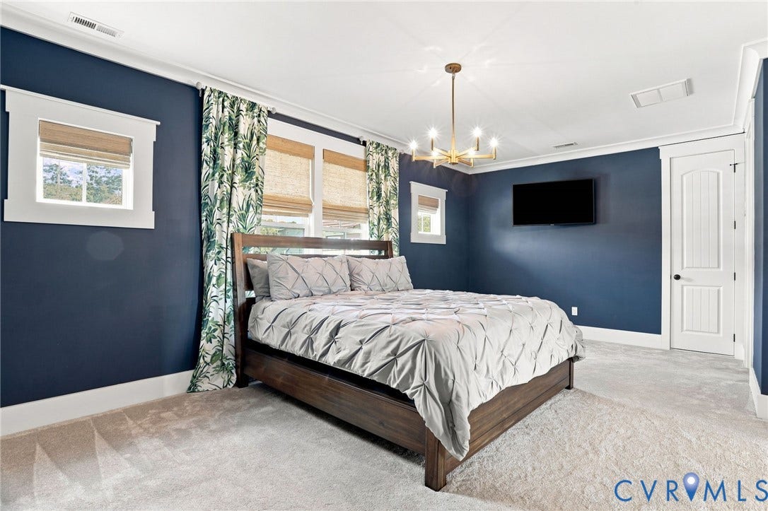 Spacious room featuring broadloom carpet, multiple windows with natural fiber shades, a modern chandelier, and a paneled interior door