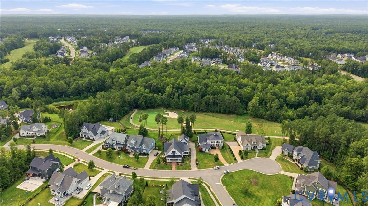 Expansive residential development featuring paved streets and varied architectural styles, bordered by mature woodlands and a golf course