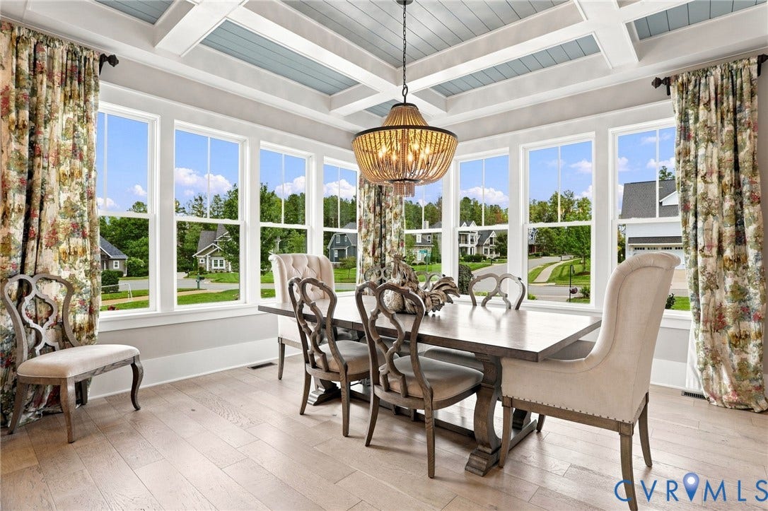 Dining area featuring a coffered ceiling with a light blue inset, light wood-finish flooring, a series of tall windows, and a decorative chandelier
