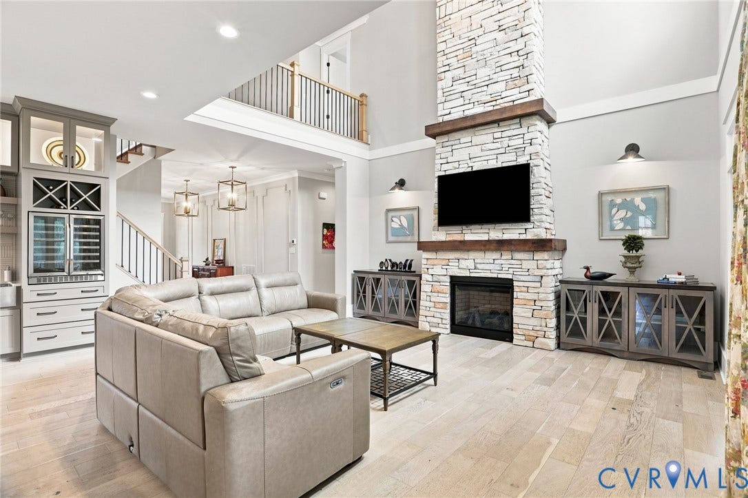 Two-story living area featuring a stacked stone fireplace with a wood mantel, built-in cabinetry with a wine cooler, and light wood-finish flooring