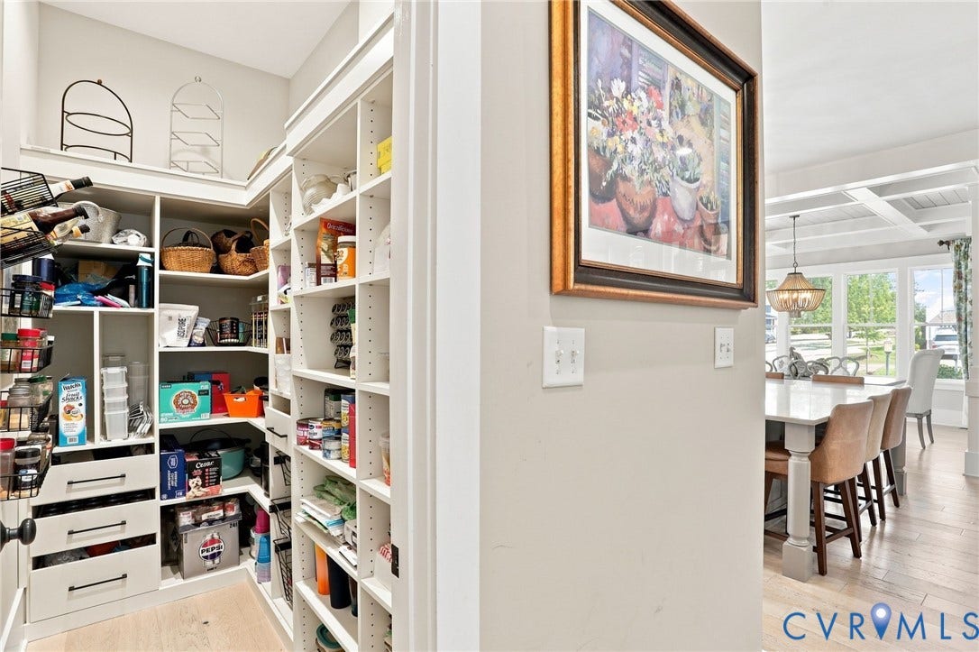 Walk-in pantry featuring extensive built-in shelving, multiple drawers with dark hardware, and light wood-finish flooring