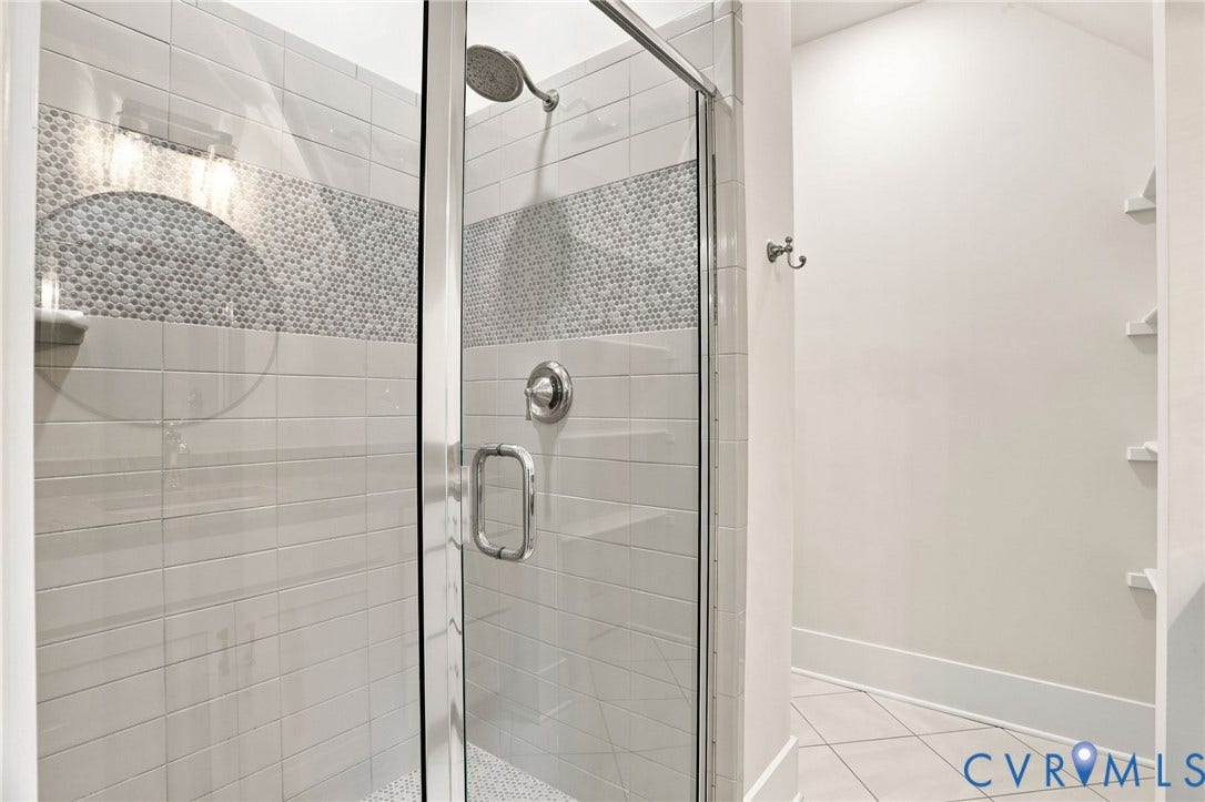 Glass-enclosed shower featuring a rainfall showerhead, chrome fixtures, horizontal subway tile, and a decorative mosaic tile accent band