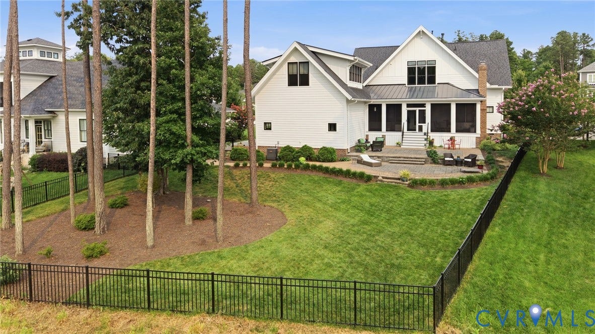 Expansive rear yard featuring a manicured lawn, established landscaping, and a black wrought iron fence