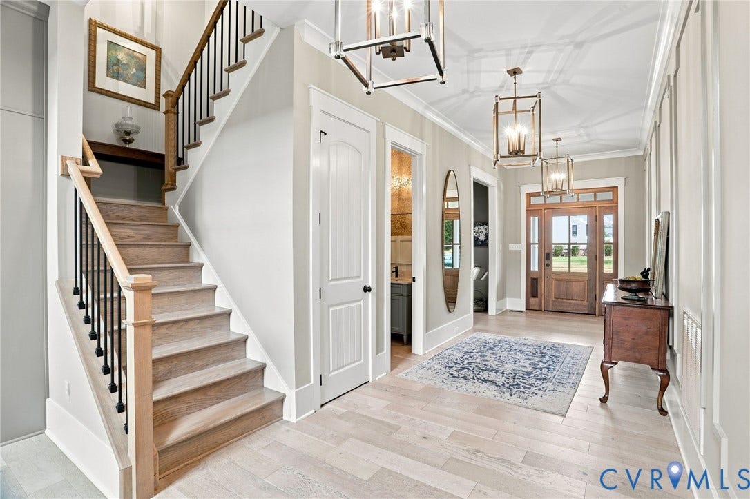 Grand entryway featuring a natural wood front door with sidelights and transom window, light wood-finish flooring, two decorative lantern pendants, and a staircase with natural wood handrails and black iron balusters