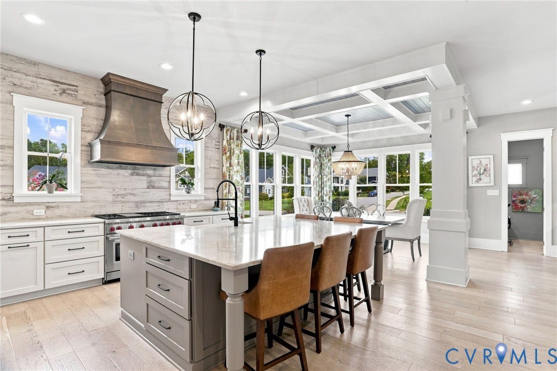 Gourmet kitchen with a large center island featuring stone countertops, a professional-grade range with a custom range hood, and light wood-finish flooring