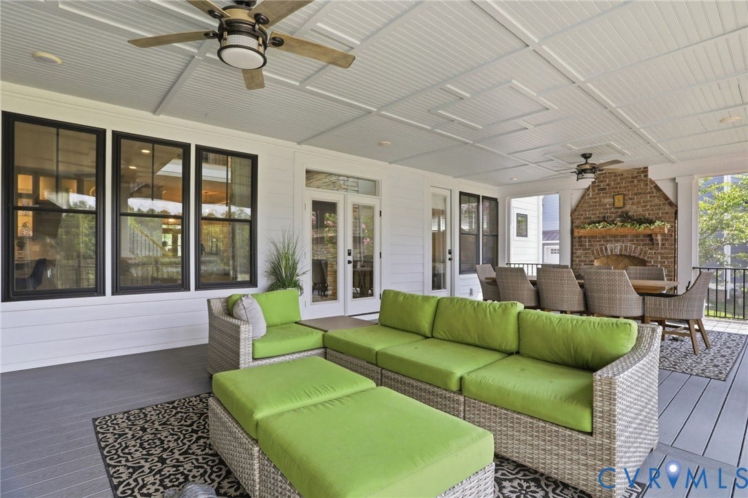 Expansive covered porch featuring a brick fireplace, patterned coffered ceiling, two ceiling fans, and multiple black-framed windows