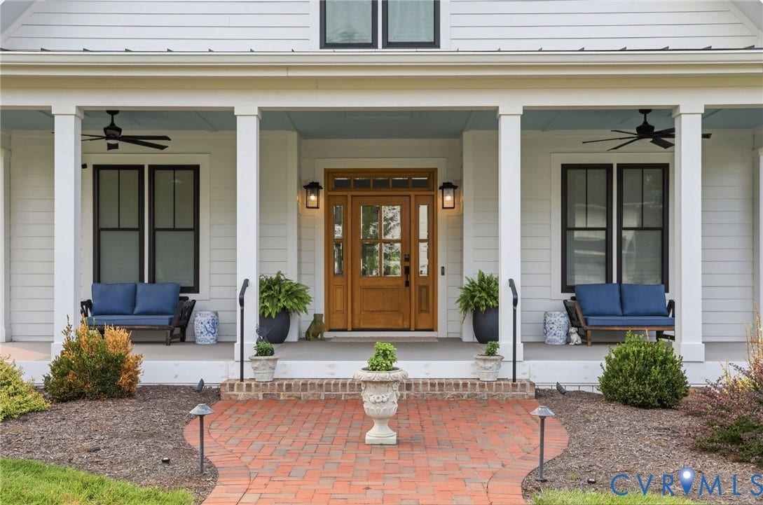 Welcoming front porch featuring a natural wood entry door with glass panels, flanked by two wall-mounted lanterns and black-framed windows