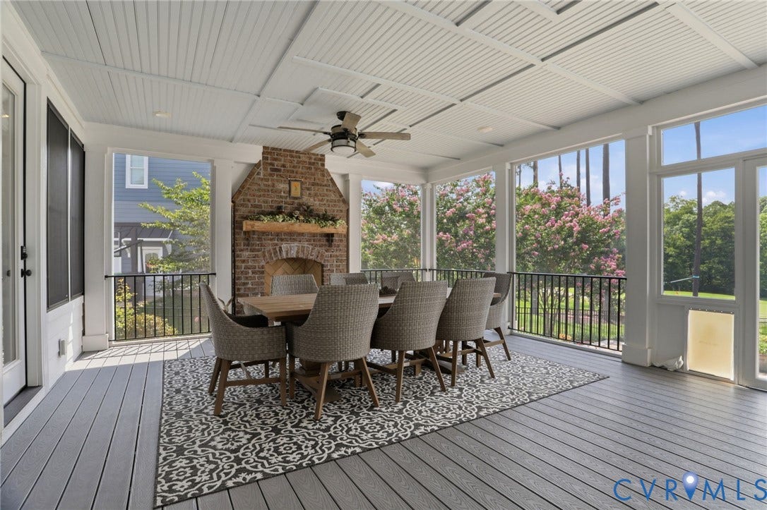 Spacious screened porch featuring a brick fireplace with a wood mantel, a wood-finish dining table, and a ceiling fan