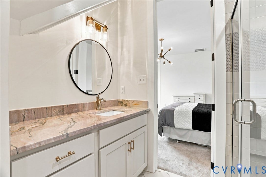 Bathroom vanity with a stone countertop, a round mirror, and a gold-finish faucet