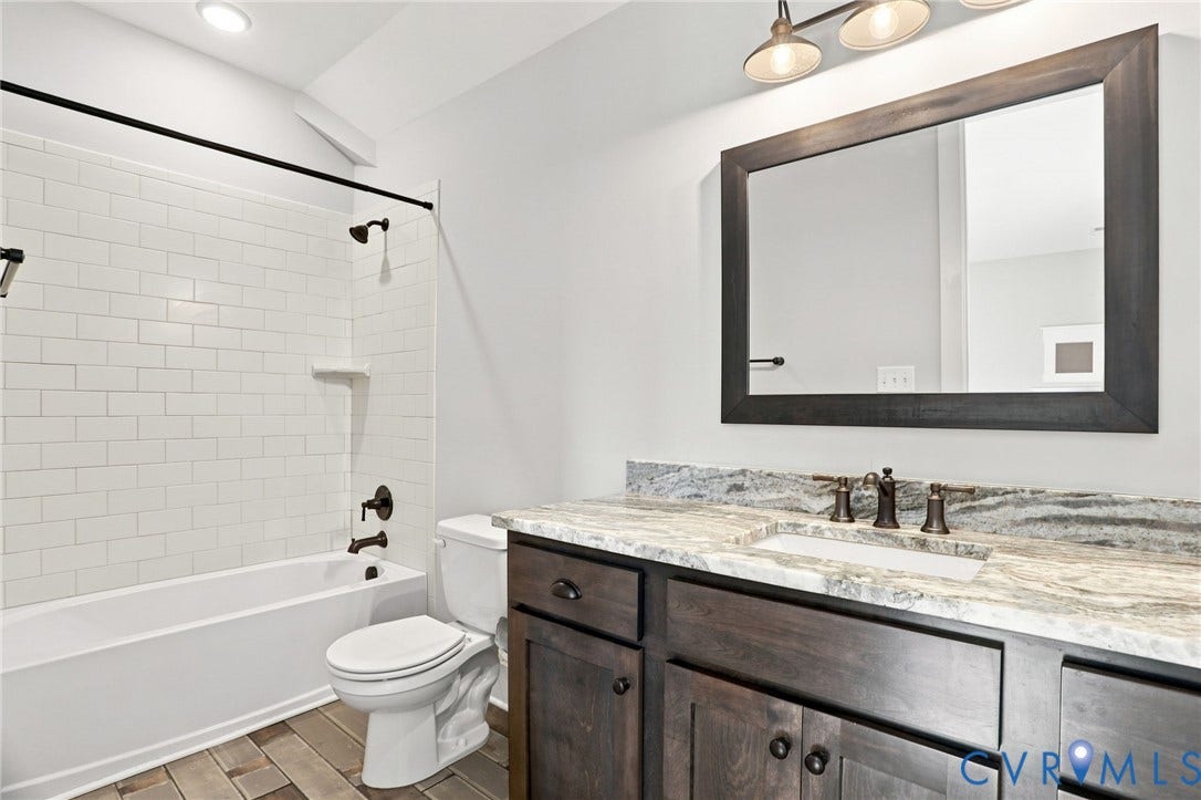 Bathroom featuring a built-in tub with subway tile surround, dark wood-finish vanity with an integrated sink, stone countertop, and wood-finish flooring