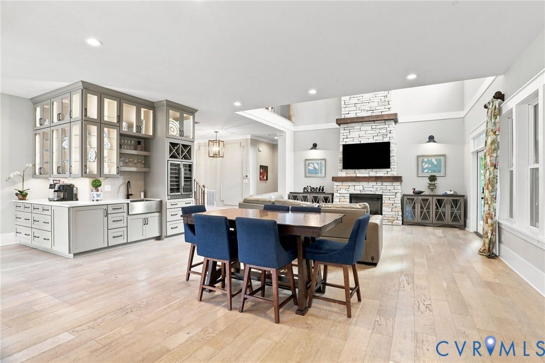 Spacious open-concept living area featuring light wood-finish flooring, a stone-clad fireplace with a wood mantel, and a built-in wet bar with glass-front cabinetry and a beverage cooler