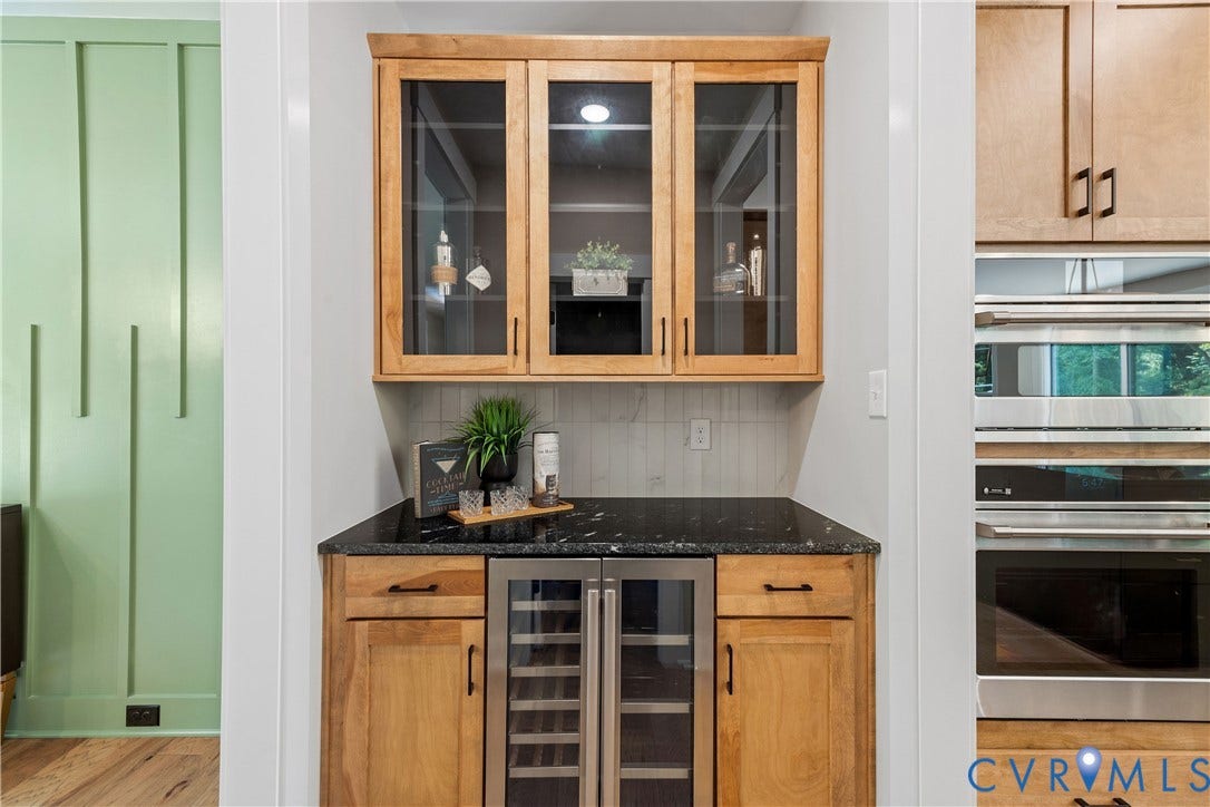 Built-in wet bar featuring natural wood cabinetry, a dark stone countertop, a tiled backsplash, and glass-front upper cabinets