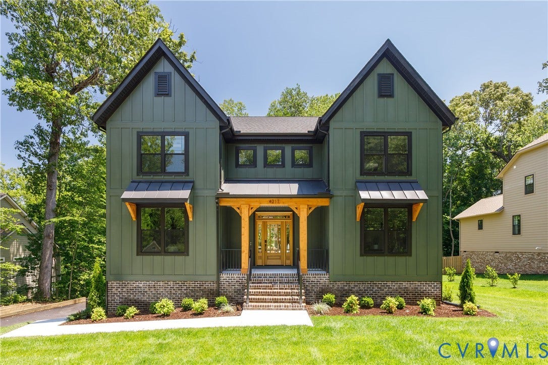 Modern farmhouse exterior featuring board and batten siding, dark trim windows, natural wood porch accents, a metal awning over lower windows, and a brick foundation