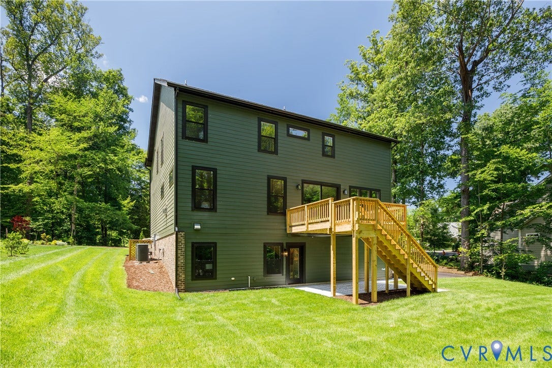 Rear exterior featuring a spacious wooden deck, a ground-level concrete patio