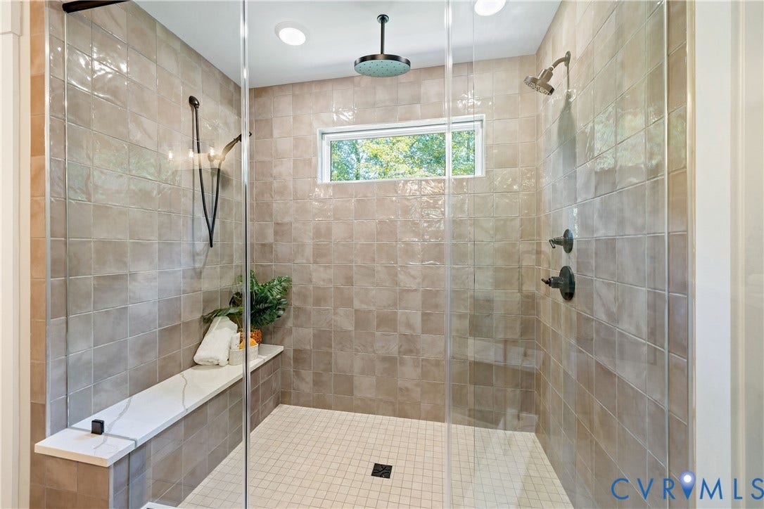 Spacious shower enclosure featuring full-height tiled walls, a built-in bench with a light-toned surface, a rainfall showerhead, and an additional wall-mounted showerhead