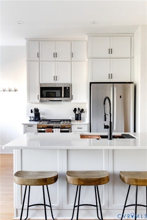 3142 Floyd Avenue, Museum District, Richmond, VA 23221 Kitchen featuring white shaker-style cabinetry, stainless steel appliances, a white countertop island with paneling, and a black faucet at the sink