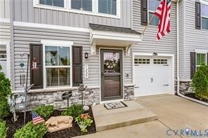7225 Lyon Taylor Lane, The Groves At New Kent, New Kent, VA 23124 Multi-level townhouse exterior featuring light gray horizontal siding, a covered entry, an attached garage, dark window shutters, and stone veneer accents