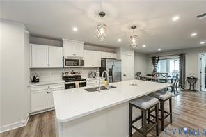 7225 Lyon Taylor Lane, The Groves At New Kent, New Kent, VA 23124 Kitchen featuring a large center island with seating, white cabinetry, integrated stainless steel appliances, and wood-finish flooring