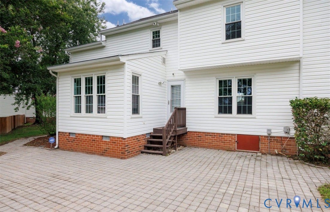 2912 Appleford Drive, Longmeadow, Chester, VA 23831 Expansive paver patio with a white vinyl siding exterior featuring multiple windows with grid patterns, a brick foundation, and exterior stairs with a wooden railing leading to a white door