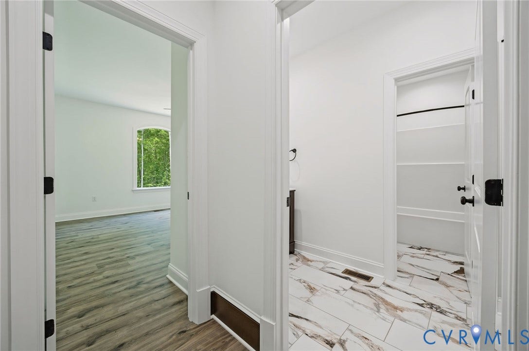 6995 Jefferson Highway, Louisa, VA 23117 Hallway featuring white doors with dark hardware, leading to a room with wood-finish flooring and a large arched window