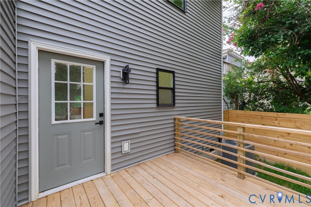 1514 Custer Street, Richmond, VA 23222 Expansive wood-finish deck with horizontal slat railings, featuring a panel-style door with a divided light window, gray siding, and an exterior wall sconce
