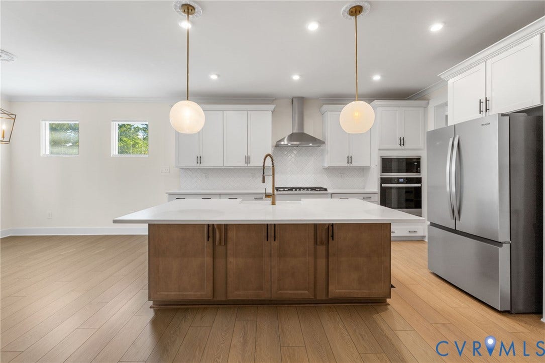 Kitchen featuring a central island with a solid surface countertop, stainless steel appliances, white upper cabinetry, and wood-finish flooring