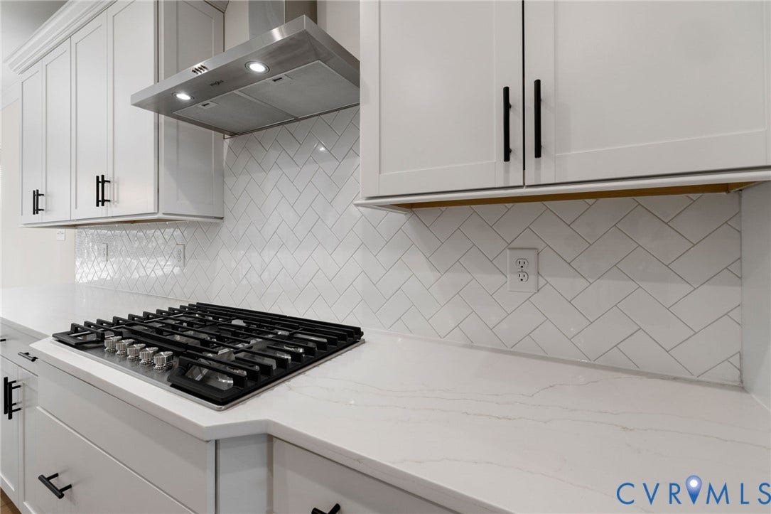 White cabinetry with matte black hardware, stainless steel range hood, white herringbone tile backsplash, and light-toned countertops