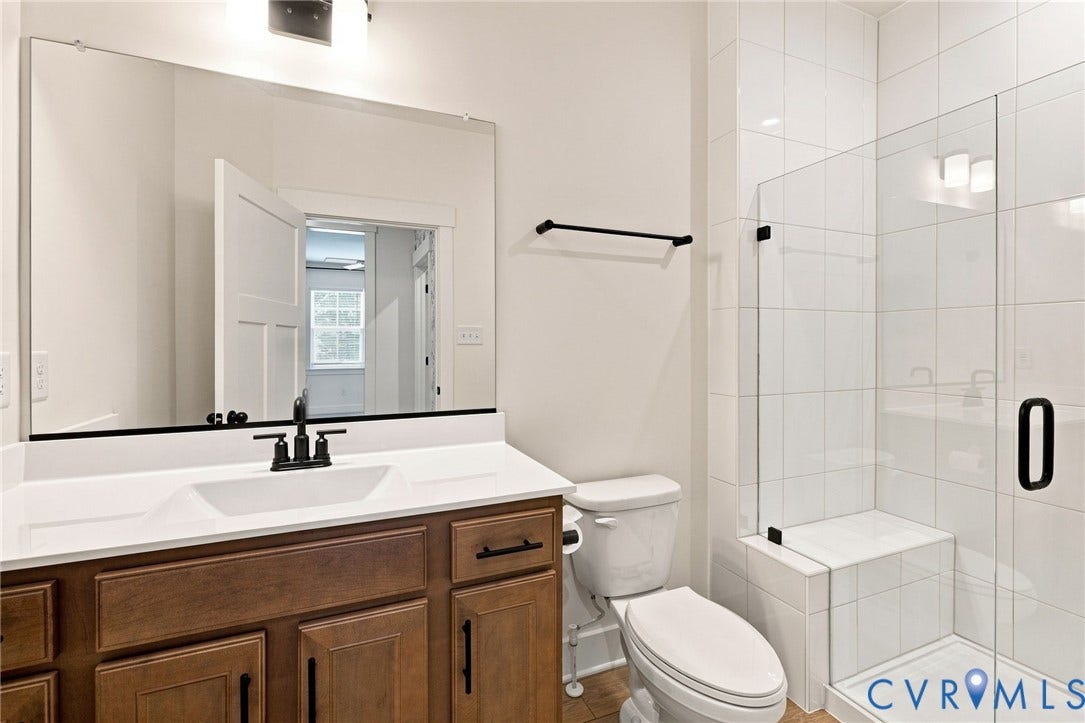 Wood-finish vanity with an integrated sink, broad mirror, walk-in shower with clear glass enclosure, and white tile surround