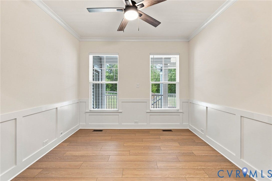Wood-finish flooring, white board and batten wall treatment, crown molding, two windows with blinds, and a ceiling fan with integrated lighting