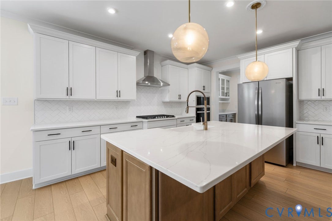 Contemporary kitchen featuring white cabinetry, a large center island with a stone countertop, stainless steel appliances, and wood-finish flooring