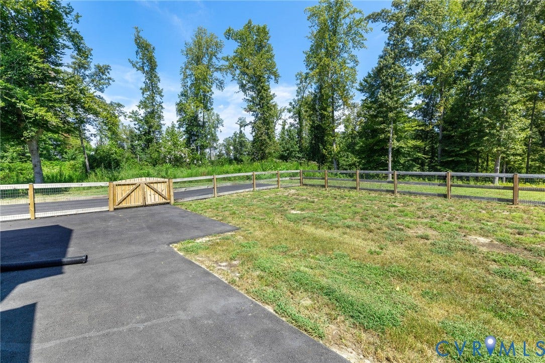 Paved driveway with a wooden gate, split-rail fence, and mature trees bordering the property