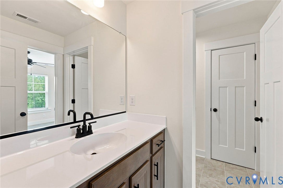 Jack and Jill bath between bedrooms. White countertop with an integrated oval sink and black-finish faucet