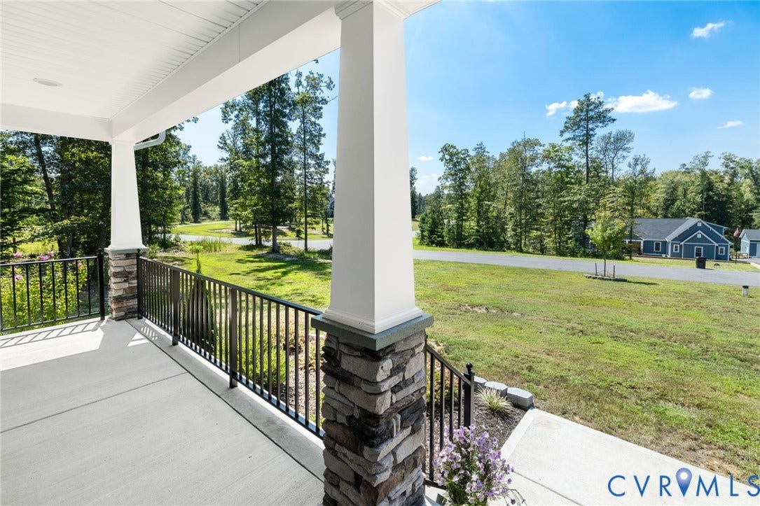 Covered front porch with stone-clad columns, white paneled ceiling, and black metal railings