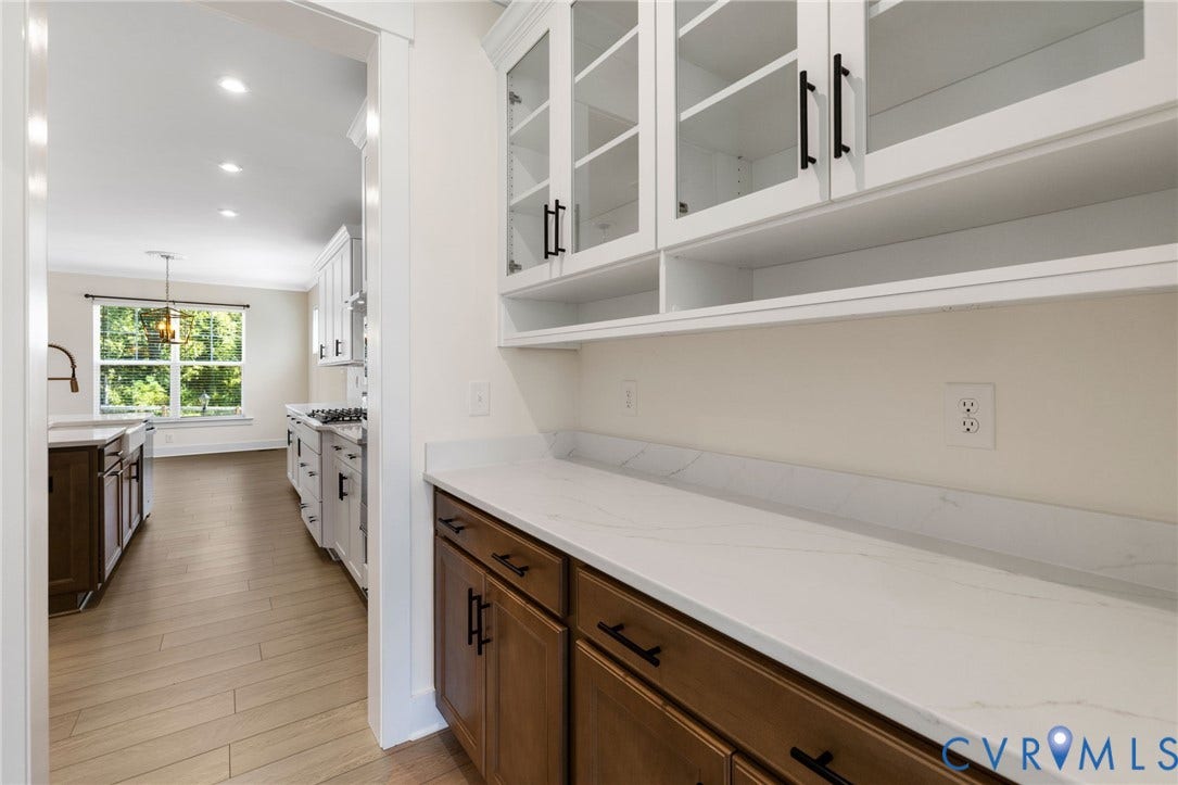 Butlers Pantry, White upper cabinetry with glass inserts, wood-finish lower cabinetry, light-toned countertops, and wood-finish flooring
