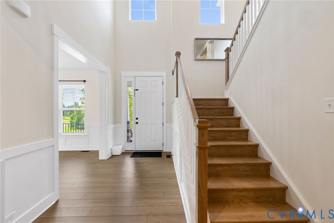 Two-story entry foyer with wood finish flooring, white paneled wainscoting, and a prominent staircase with wood newel posts and handrail