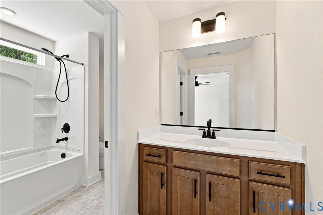 Jack and Jill bath between bedrooms. Wood-finish vanity with solid surface countertop and undermount sink