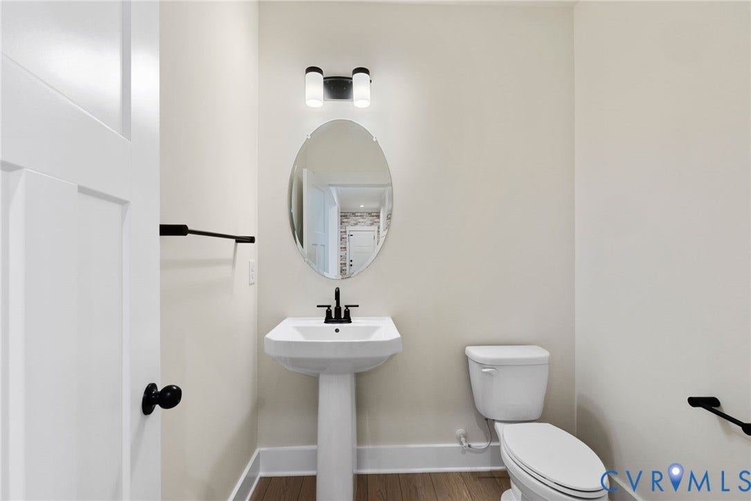 Pedestal sink with matte black faucet, wall-mounted oval mirror, modern black and white light fixture, white toilet, and wood-finish flooring