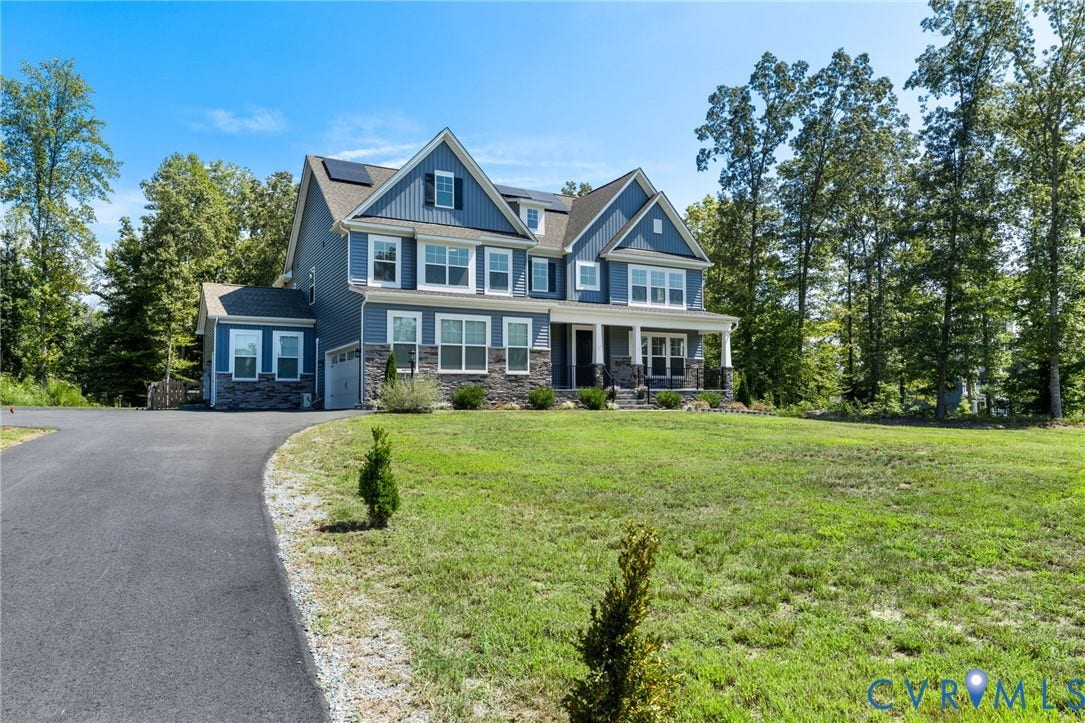 Two-story residential structure featuring blue siding, stone veneer accents, an attached garage, and a covered front porch