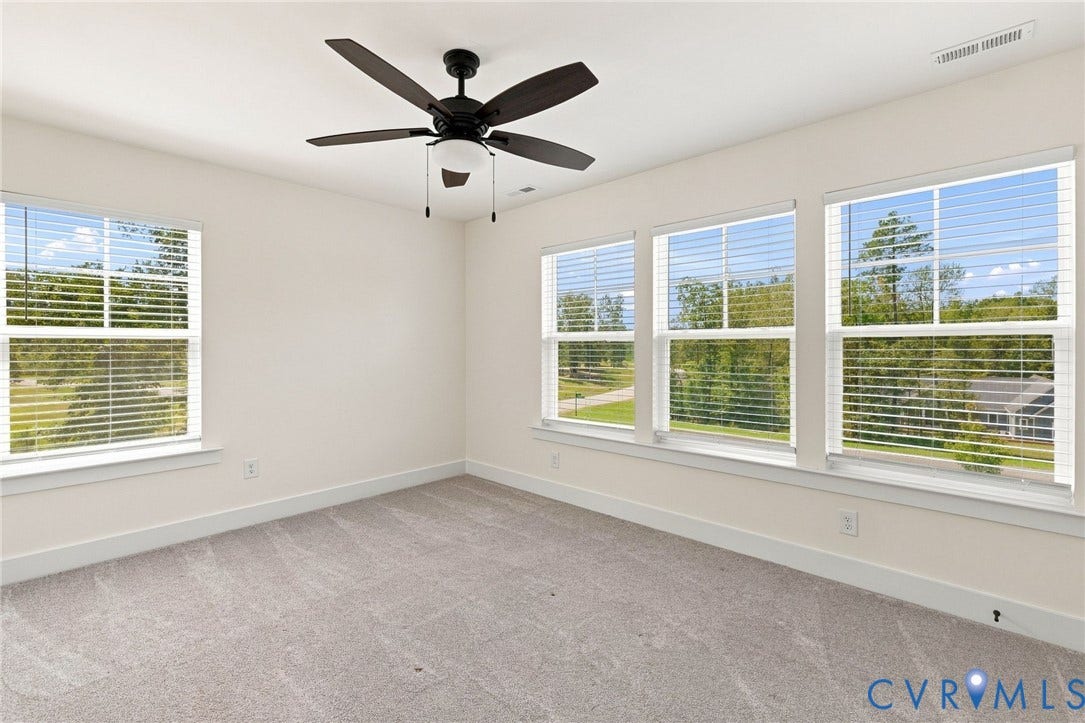 Neutral wall paint, plush carpet, multiple windows, window blinds, and a ceiling fan