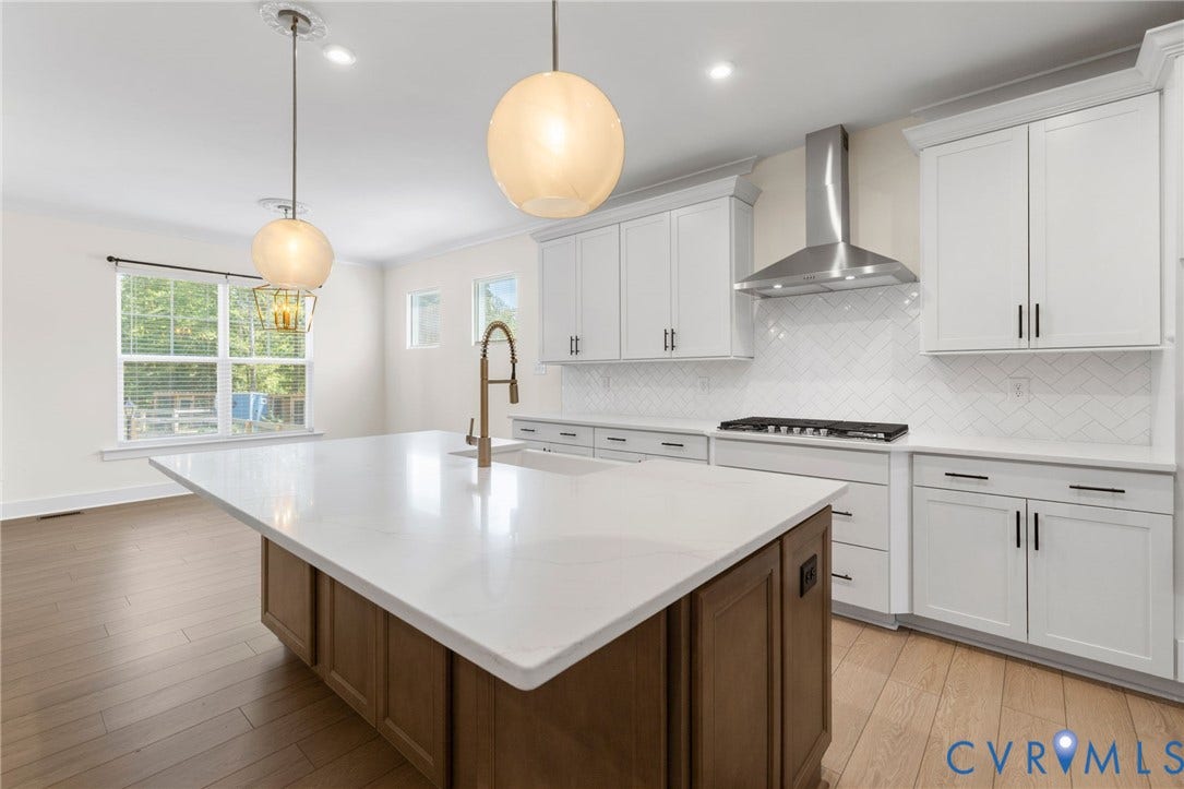Kitchen featuring wood-finish flooring, a central island with a white countertop and integrated sink, white shaker-style cabinetry, and a herringbone-patterned tile backsplash