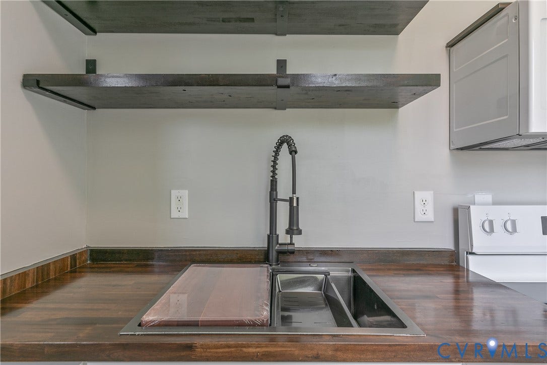 2801 4th Avenue, Richmond, VA 23222 Kitchen workstation sink with cutting board insert, dark wood-finish countertops, black gooseneck faucet, light grey wall paint, and open shelving