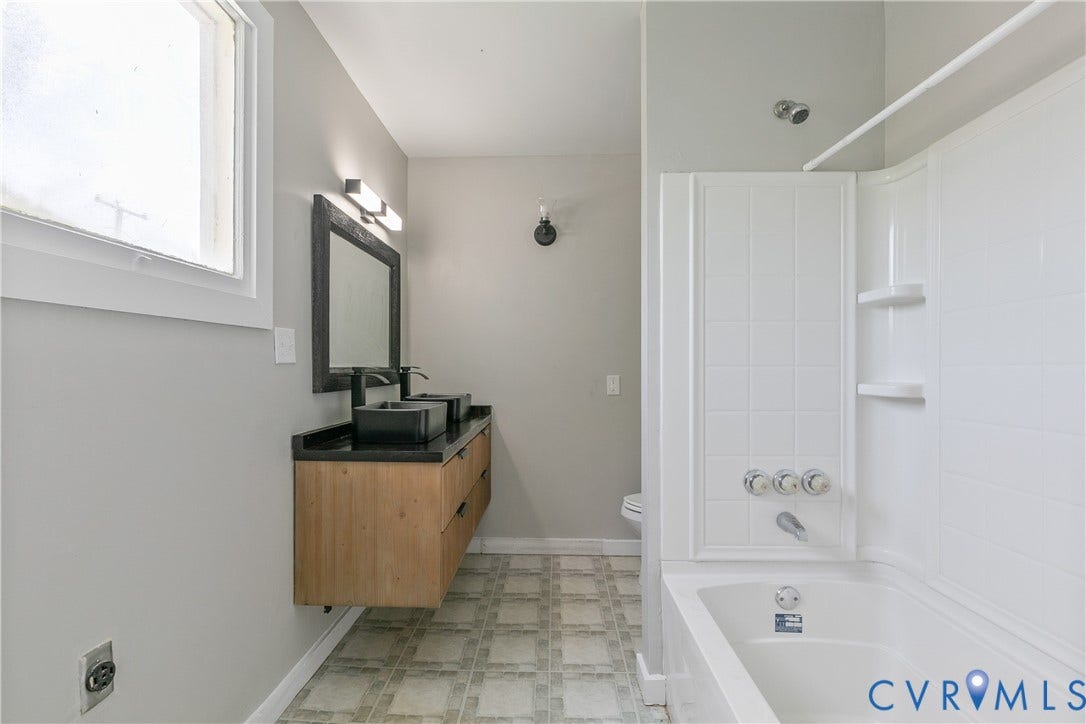 2801 4th Avenue, Richmond, VA 23222 Modern bathroom featuring a floating wood-finish vanity with dual vessel sinks, a dark countertop, and a framed mirror