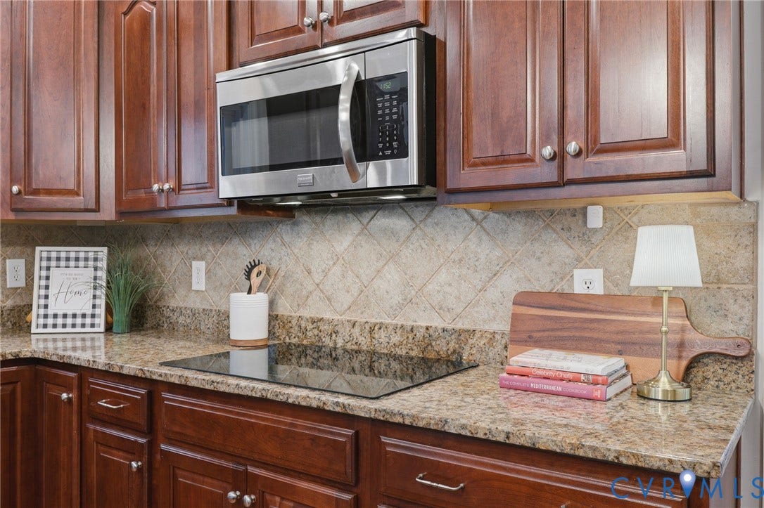 7618 Hampton Green Drive, Chesterfield, VA 23832 Rich wood cabinetry with silver hardware, granite countertops, stainless steel microwave, black electric cooktop, and diamond-patterned tile backsplash