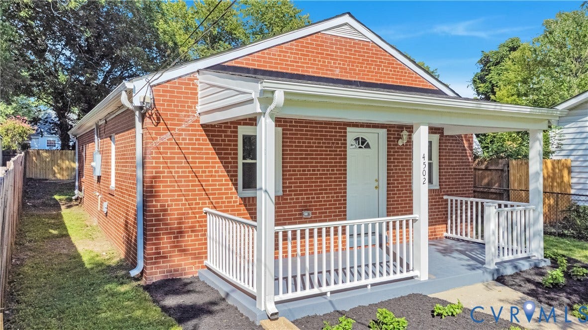 4502 Bunn Avenue, Fulton, Richmond, VA 23231 Brick facade residence featuring a covered front porch with white railings, a new white entry door with an arched window, and exterior lighting fixtures
