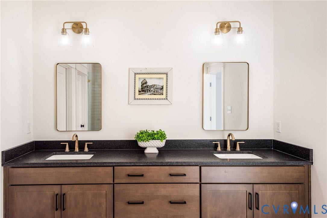 Dual vanity featuring dark stone countertops and wood-finish cabinetry