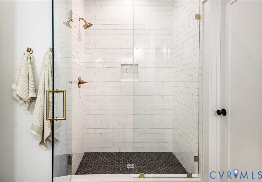 Frameless glass shower enclosure featuring brass hardware, subway tile surround, dark hexagonal tile flooring, and a recessed shower niche