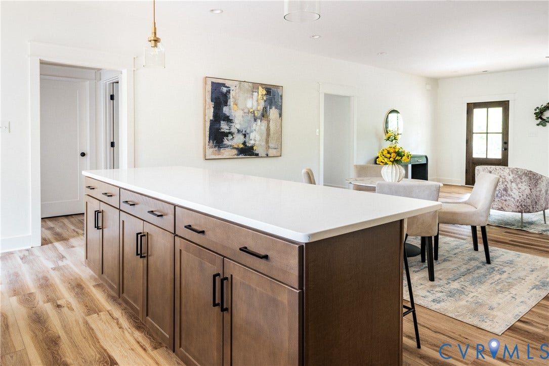 Kitchen island with a white countertop and wood-finish cabinetry, featuring integrated seating and dark hardware